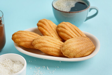 Plate with delicious madeleines, cup of coffee and coconut flakes on blue background