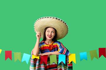 Happy young woman in Mexican clothes and with garland pointing at something on green background