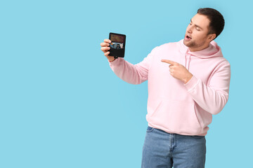 Young man pointing at wallet with gift card on blue background