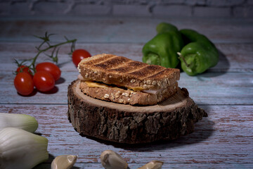 Toasted cheese and turkey sandwich on rustic table with cherry tomatoes, peppers, chives and garlic
