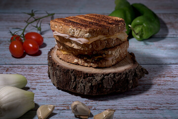 Toasted cheese and turkey sandwich on rustic table with cherry tomatoes, peppers, chives and garlic