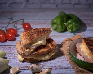Toasted cheese and turkey sandwich on rustic table with cherry tomatoes, peppers, chives and garlic