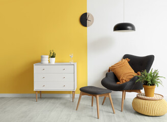 Interior of stylish living room with black armchair, chest of drawers, lamp and clock on yellow wall