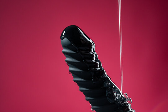 Lube pouring on black dildo on pink background. 