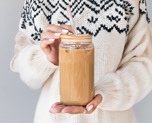 Girl is holding glass can in hands. (Only background modified with AI) Blank 16 oz Glass Can with lid, straw and coffee woman mockup .Girl is holding bottle in hands with sweater, Sublimation