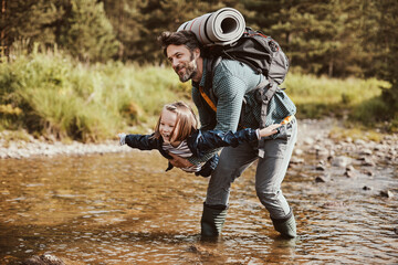 Father carrying his daughter over a creek while they are out hiking in the forest
