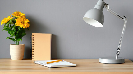 Minimalist workspace with yellow flowers, notebook, lamp, wooden desk, and gray wall