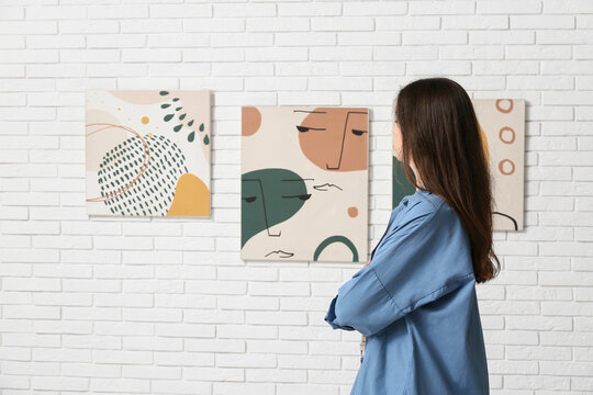 Young woman looking at paintings on white brick wall in art gallery