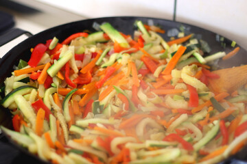 Stir frying chopped leek, zucchinis, carrots and red bell peppers in a wok. Selective focus.