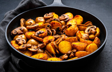 Boiled and fried potatoes in peels with champignon mushrooms and spices in frying pan. Black background, top view