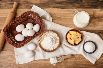 Bowl of flour with scoop, eggs, jug of milk and butter for preparing dough on wooden background