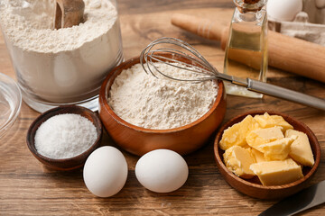 Flour in jar with eggs, butter and whisk for preparing dough on wooden background