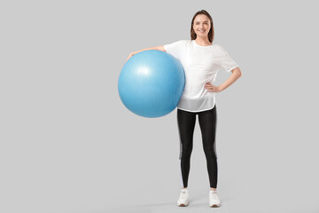 Fototapeta premium Sporty young woman with fitball on grey background