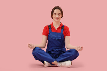 Young female construction worker meditating on pink background