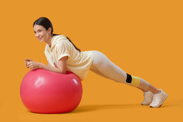 Sporty young woman exercising with fitball on yellow background