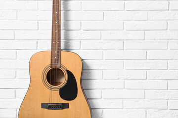 Obraz premium Modern acoustic guitar hanging on white brick wall, closeup