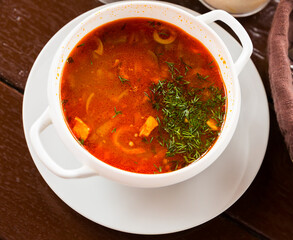 Tasty meat soup with assorted meat, olives and pickled cucumbers served with herbs in white bowl