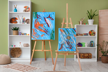 Interior of artist's workshop with paintings on easels and art supplies in shelving units