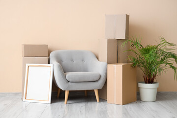 Cardboard boxes with grey armchair and houseplant near beige wall in living room on moving day