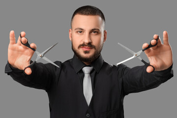 Handsome young bearded man with scissors on grey background