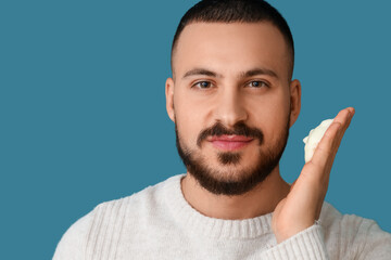 Obraz premium Handsome young bearded man applying face wash foam on blue background