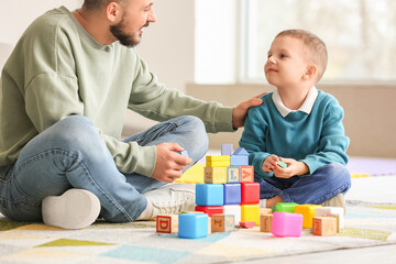 Happy father and his little son playing with colorful cubes on floor at home