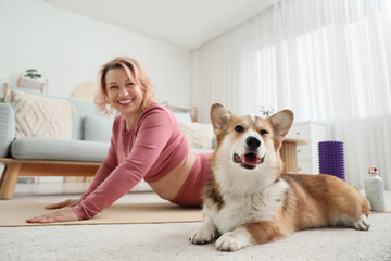 Beautiful happy mature sporty woman practising yoga with cute Corgi dog at home