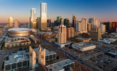 High-angle view of Edmonton downtown core at sunset. Modern skyscrapers and the Areana are prominent. Urban activity is visible with cars and buses on the streets. Edmonton, Alberta, Canada