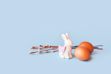 Spring easter holiday, decorative composition with willow branch, white statuette rabbit and colorful painted eggs on pastel light blue background. Isolated, front view, place for text