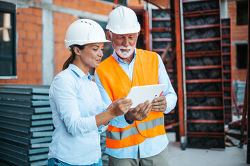 Construction Professionals Discuss Blueprints Using a Digital Tablet on a Building Site
