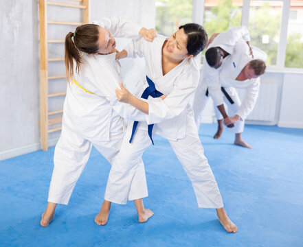 Adult woman and young female judoka practicing judo technique in group in gym