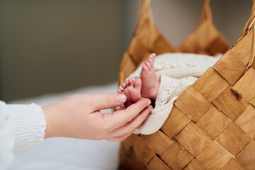 A tender close up of a babys tiny feet resting in a woven basket while an adult hand gently holds...