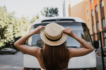 A girl in a straw hat stands in front of a vintage van on a sunny day in the city