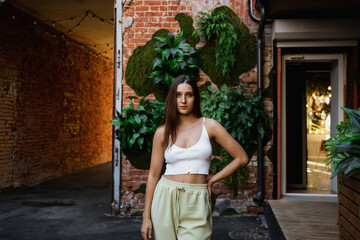 Stylish young woman posing confidently in an urban alley adorned with greenery in the late afternoon glow