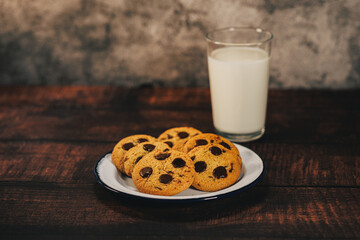 A plate of freshly baked chocolate chip cookies served with a glass of milk in a rustic setting. Ideal for dessert, snack, or homemade baking themes