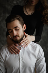 The girl stands behind the guy and hugs his neck