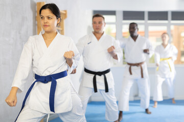 Diligent middle-aged woman attendee of karate classes practicing kata standing in row with others...