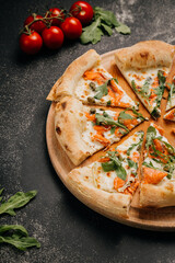 Sliced gourmet pizza with smoked salmon, arugula, and capers on a rustic wooden board