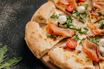 Delicious prosciutto and arugula pizza with cherry tomatoes and mozzarella on a wooden platter