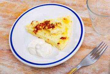 Delicious and dietary homemade food, piece of cottage cheese casserole is on plate. Dish is complemented with sour cream. Top view, breakfast served.