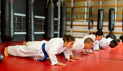 Men and women wearing kimono and doing push-ups in gym during group karate training.