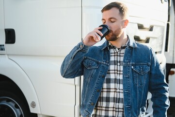 The truck driver drinks coffee. The truck driver rests in the parking lot after work