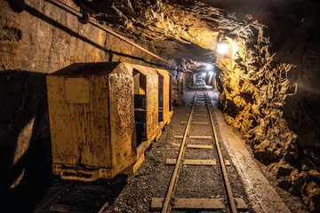 Inside the historic mine shaft of Jachymov, rusty mine carts sit on the tracks, illuminated by dim...