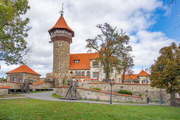 Fototapeta premium Hnevin Castle stands majestically in Most, Czechia, showcasing its stunning architecture against a backdrop of trees and clouds. Visitors can explore the surrounding grounds and enjoy the serene park.