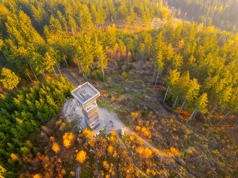 The Cisarsky Kamen wooden lookout tower stands majestically amidst vibrant autumn foliage, offering stunning views as the sun sets over the tranquil landscape near Liberec.