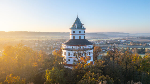 The elegant Baroque hunting chateau of Humprecht stands majestically above Sobotka as the sun rises, illuminating the vibrant autumn foliage and tranquil landscape of the Bohemian Paradise.