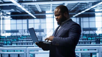 Computer scientist in server hub checking recovery plan on laptop, monitoring hardware energy...