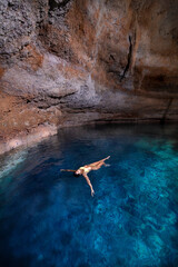 Mujer joven, atractiva, latina en bikini, flotando/nadando en un cenote cristalino, azul turquesa, cerca de Tulum México