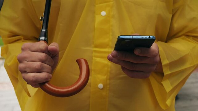 Using phone taxi app during rain, Unrecognizable man standing on the city streets under umbrella and using cellphone