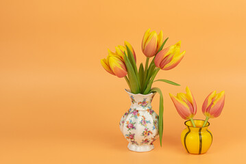Wunderschöne gelb-orange farbende Tulpen in zwei Vasen vor einen orangen Hintergrund, Platz für Text
